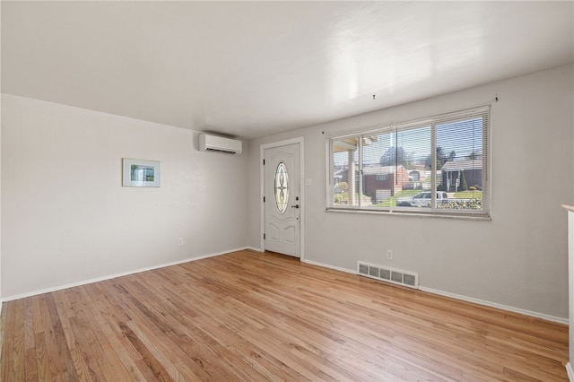 foyer featuring light wood-style floors, baseboards, a wall mounted AC, and visible vents