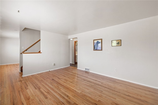 unfurnished room featuring baseboards, visible vents, stairway, and light wood-type flooring