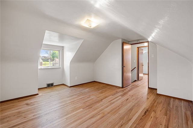 additional living space with light wood-style floors, baseboards, lofted ceiling, and visible vents