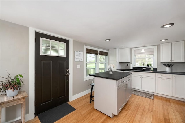 kitchen featuring dark countertops, a sink, light wood finished floors, white cabinetry, and a kitchen island