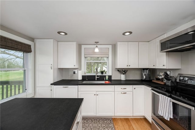 kitchen featuring dark countertops, appliances with stainless steel finishes, a sink, white cabinetry, and light wood-type flooring