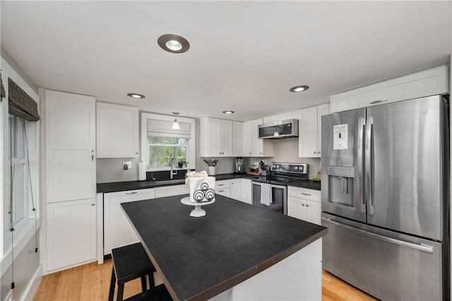 kitchen with dark countertops, white cabinets, a sink, light wood finished floors, and stainless steel appliances