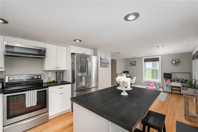 kitchen with dark countertops, range hood, white cabinets, light wood finished floors, and stainless steel appliances