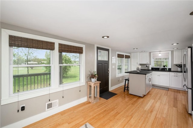 kitchen featuring visible vents, a center island, white cabinets, freestanding refrigerator, and light wood-style floors