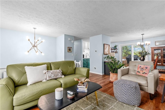 living area featuring baseboards, a textured ceiling, a notable chandelier, and wood finished floors