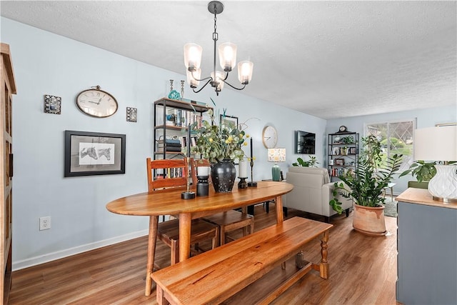 dining space with baseboards, a textured ceiling, a notable chandelier, and wood finished floors