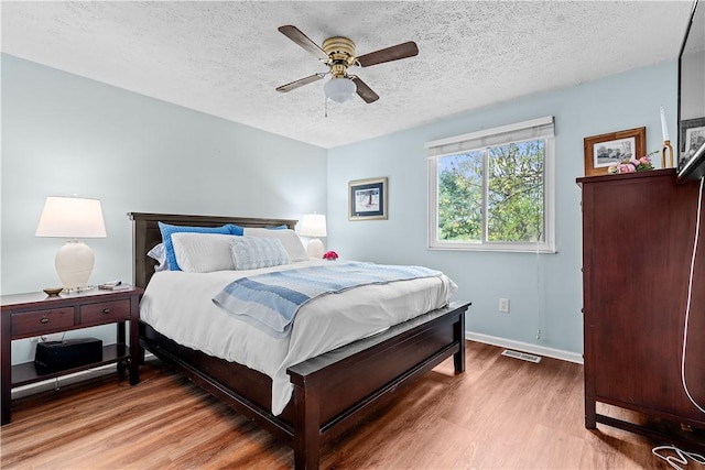 bedroom with ceiling fan, a textured ceiling, visible vents, baseboards, and light wood-style floors