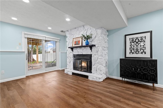 unfurnished living room with baseboards, a textured ceiling, wood finished floors, and a stone fireplace