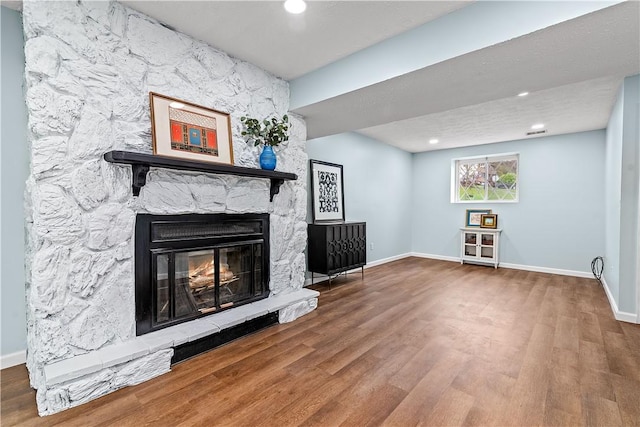 unfurnished living room with baseboards, recessed lighting, wood finished floors, and a stone fireplace