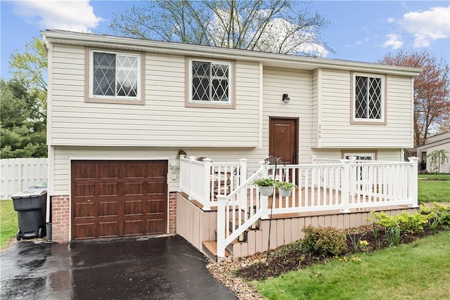 bi-level home with an attached garage, aphalt driveway, and a wooden deck