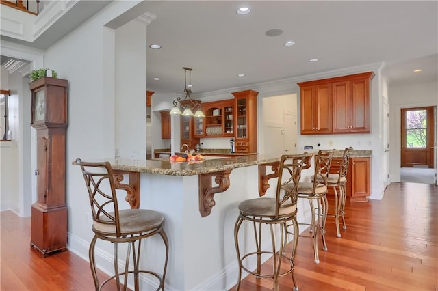 kitchen with light stone countertops, light wood-style floors, a breakfast bar area, brown cabinetry, and glass insert cabinets