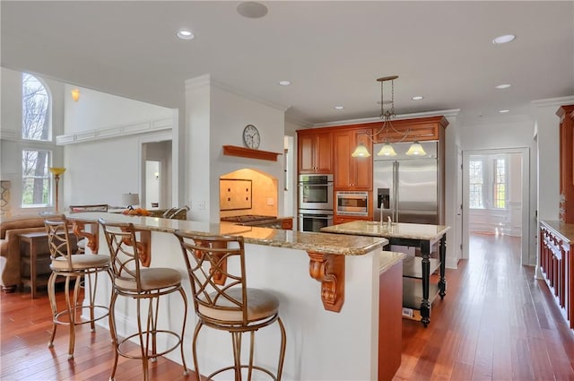 kitchen featuring light stone counters, built in appliances, a wealth of natural light, and a kitchen bar