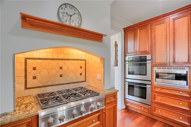 kitchen with backsplash, wood finished floors, light stone counters, ornamental molding, and stainless steel appliances