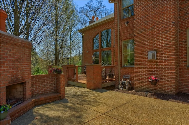 view of side of property with brick siding, a patio, a wooden deck, and an outdoor brick fireplace