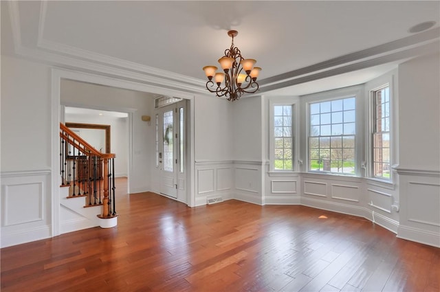 unfurnished dining area featuring visible vents, wood finished floors, a chandelier, a decorative wall, and stairs