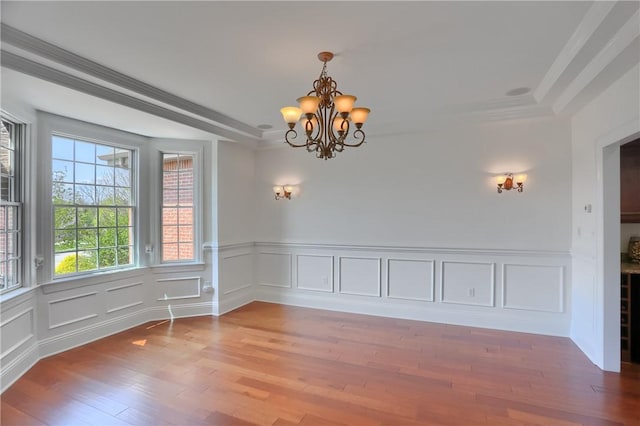 unfurnished dining area with crown molding, a decorative wall, wood finished floors, and a notable chandelier