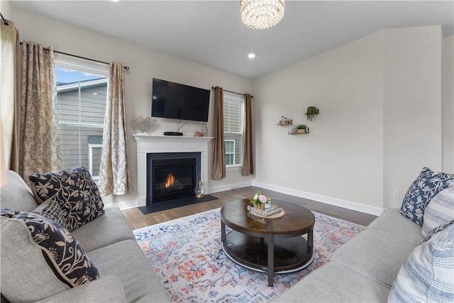 living area featuring wood finished floors, baseboards, recessed lighting, a fireplace with flush hearth, and a notable chandelier