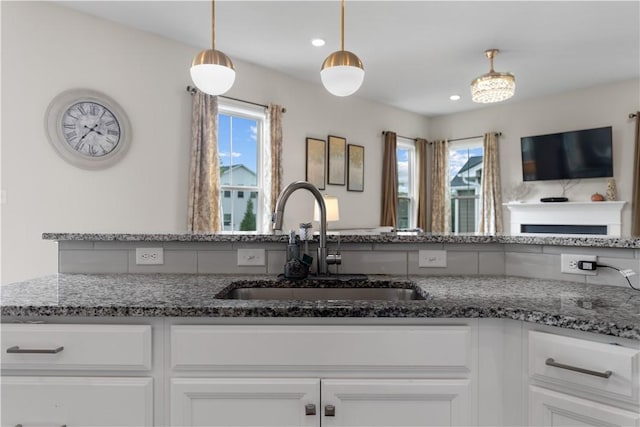 kitchen featuring a sink, white cabinets, stone counters, and a healthy amount of sunlight