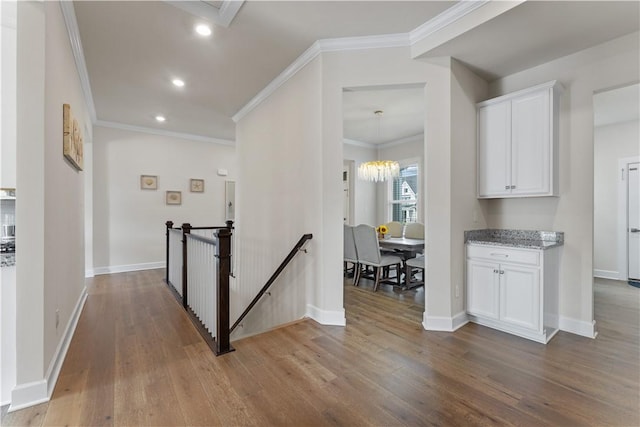 hallway with crown molding, wood finished floors, baseboards, recessed lighting, and an upstairs landing