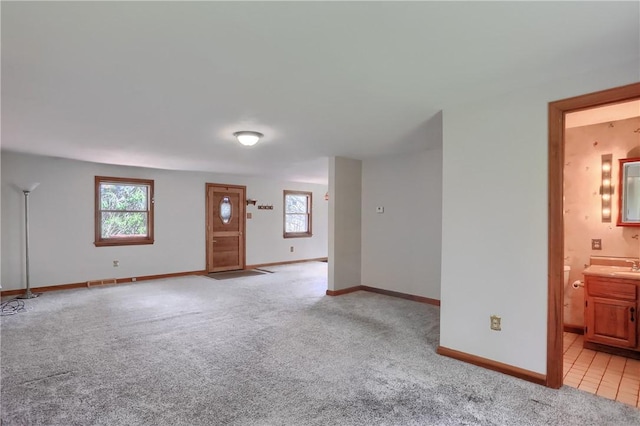 unfurnished living room featuring light colored carpet, baseboards, and a wealth of natural light
