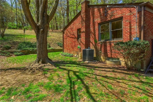 view of home's exterior featuring a lawn, brick siding, central AC unit, and a chimney