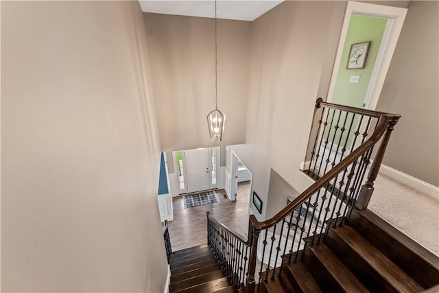 staircase with baseboards, a high ceiling, wood finished floors, and a notable chandelier