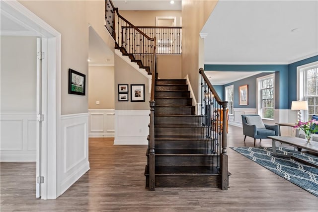 stairway featuring crown molding, a decorative wall, wood finished floors, and a wainscoted wall