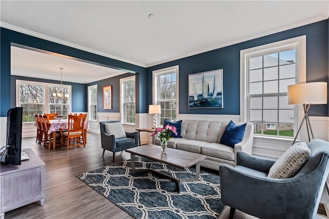 living room with an inviting chandelier, ornamental molding, wainscoting, and wood finished floors