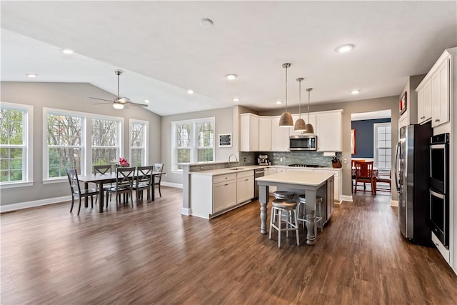 kitchen featuring a peninsula, light countertops, a sink, dark wood finished floors, and stainless steel appliances
