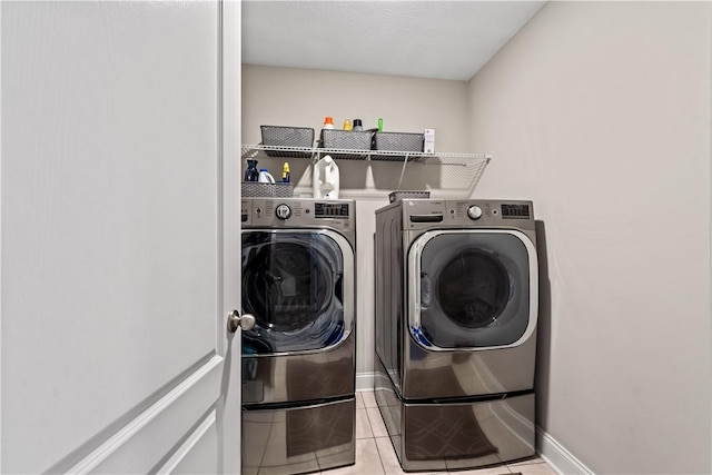 clothes washing area featuring washing machine and clothes dryer, laundry area, baseboards, and light tile patterned floors