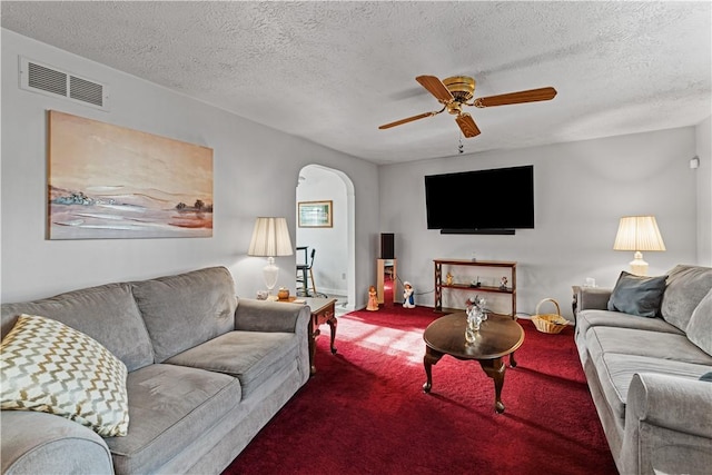 carpeted living area featuring arched walkways, ceiling fan, a textured ceiling, and visible vents