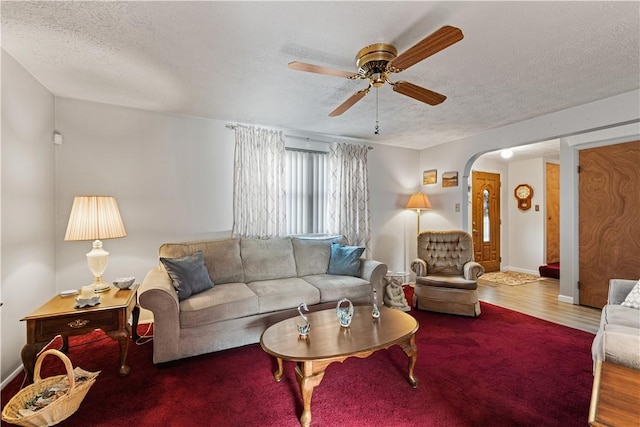 living room featuring ceiling fan, arched walkways, a textured ceiling, baseboards, and wood finished floors
