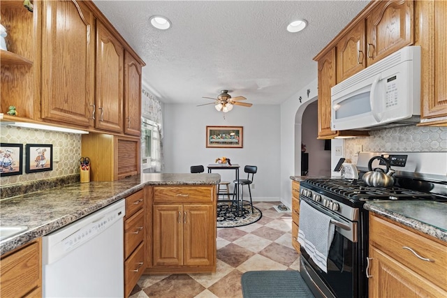 kitchen featuring white appliances, arched walkways, a textured ceiling, and ceiling fan