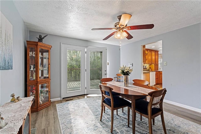 dining area featuring baseboards, a textured ceiling, light wood-style flooring, and a ceiling fan