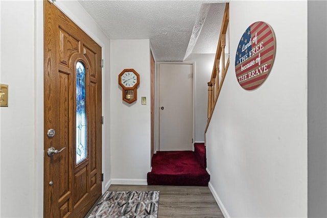foyer entrance with stairs, a textured ceiling, baseboards, and wood finished floors