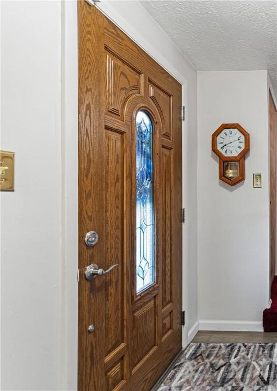 foyer featuring a textured ceiling, baseboards, and wood finished floors