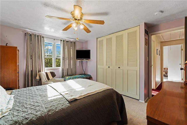 carpeted bedroom featuring a closet, visible vents, attic access, a textured ceiling, and a ceiling fan