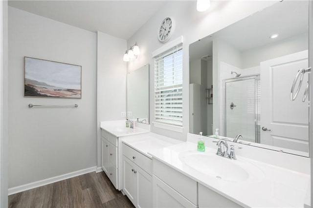bathroom featuring a sink, baseboards, two vanities, a shower stall, and wood finished floors