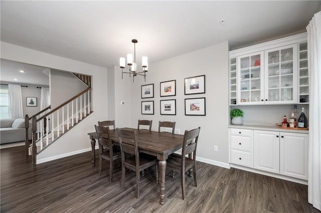 dining area featuring a chandelier, dark wood finished floors, baseboards, bar area, and stairway