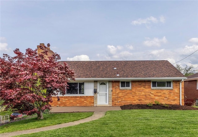 ranch-style house with roof with shingles, a chimney, a front yard, and brick siding