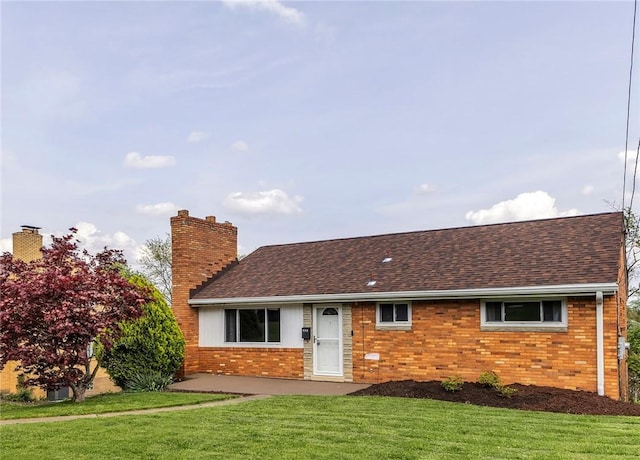 single story home with brick siding, a chimney, a shingled roof, and a front lawn