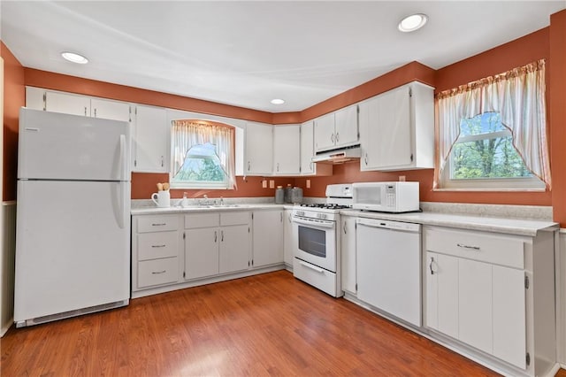 kitchen featuring light countertops, under cabinet range hood, white cabinets, and white appliances