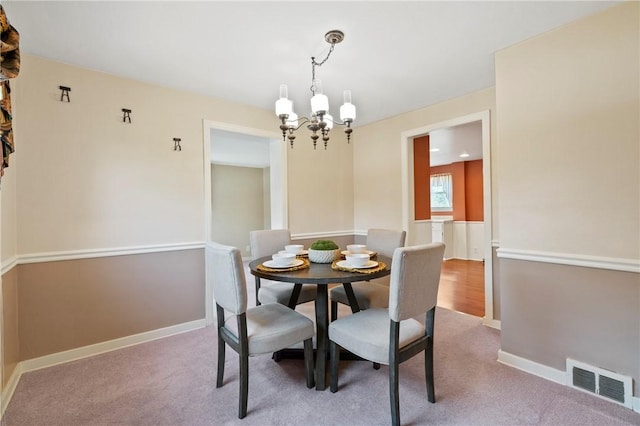 carpeted dining room featuring an inviting chandelier, baseboards, and visible vents