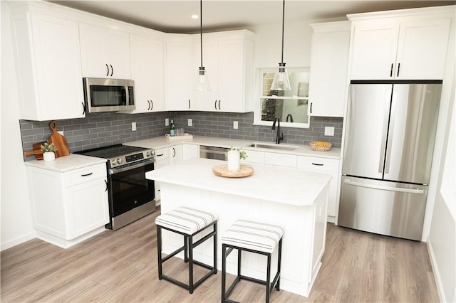 kitchen featuring decorative backsplash, light wood-style floors, a kitchen bar, a sink, and appliances with stainless steel finishes