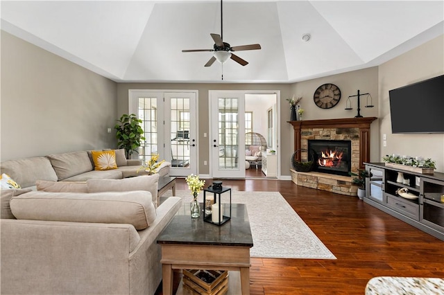 living area with a stone fireplace, a ceiling fan, dark wood finished floors, and vaulted ceiling