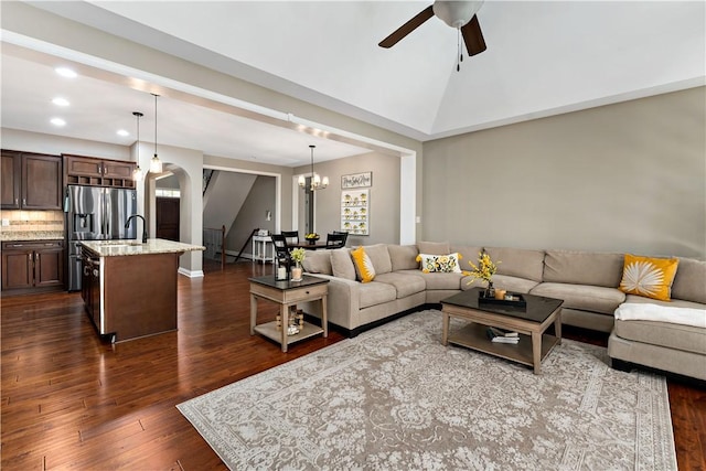 living room with arched walkways, ceiling fan with notable chandelier, dark wood-style floors, lofted ceiling, and recessed lighting
