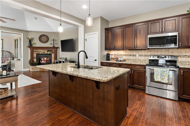 kitchen featuring appliances with stainless steel finishes, a fireplace, dark brown cabinets, a sink, and open floor plan