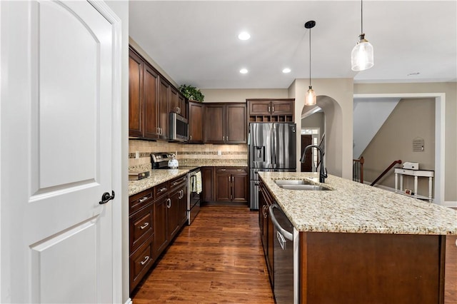 kitchen with a kitchen island with sink, dark wood-type flooring, a sink, backsplash, and stainless steel appliances