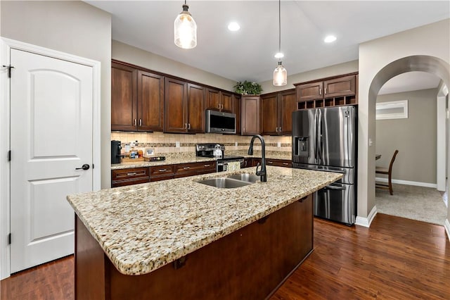kitchen with decorative light fixtures, arched walkways, dark brown cabinets, a sink, and stainless steel appliances