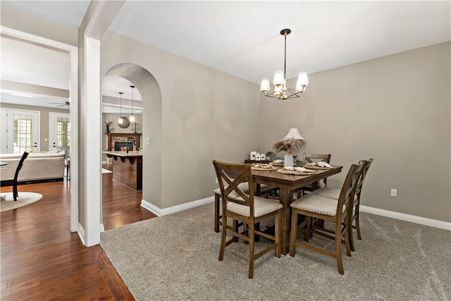 dining room with arched walkways, baseboards, ceiling fan with notable chandelier, and dark wood-style floors